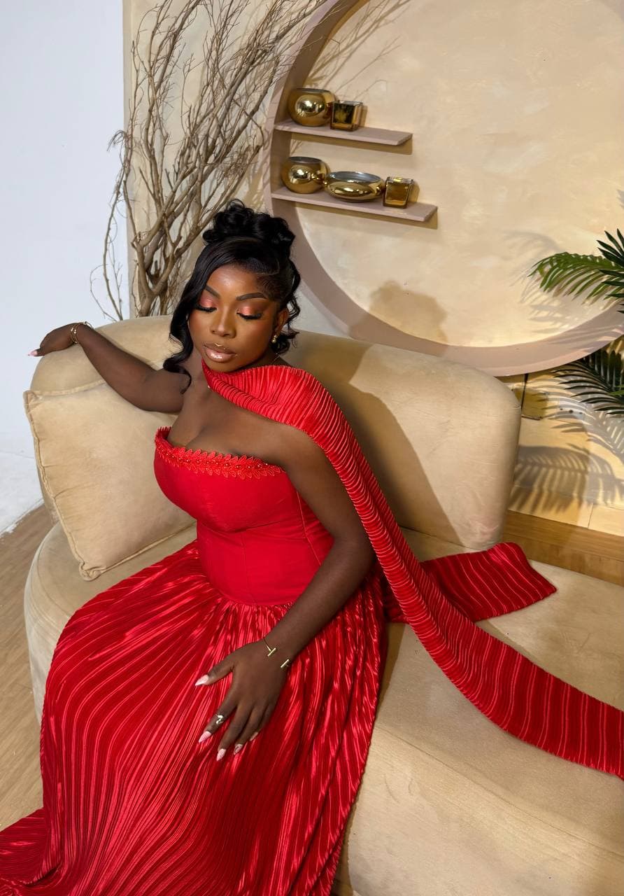 Editorial portrait in a red pleated gown, styled on a velvet chaise
